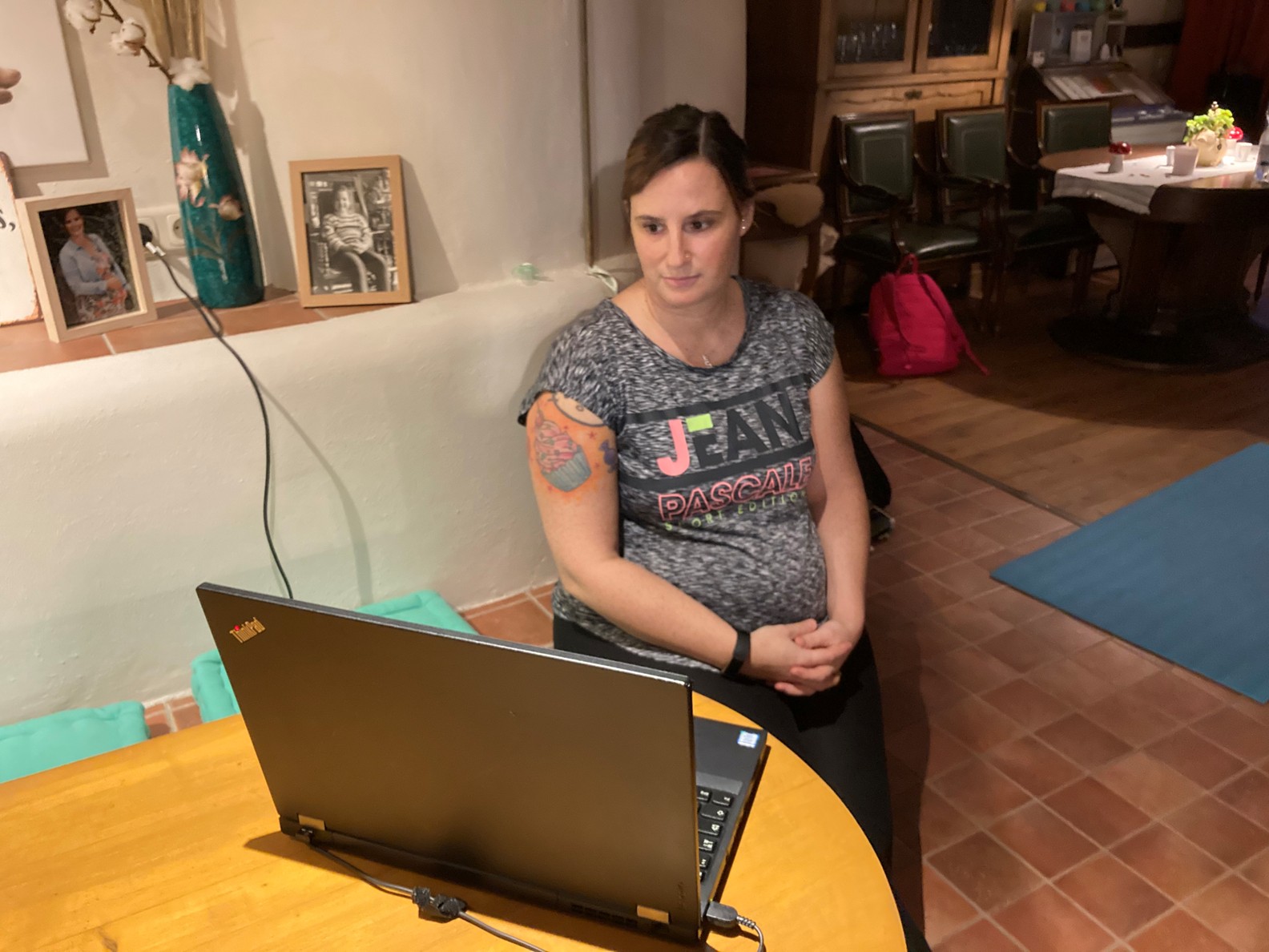 Frau mit tätowiertem Arm sitzt vor einem Laptop auf einem Tisch in einem Innenraum.