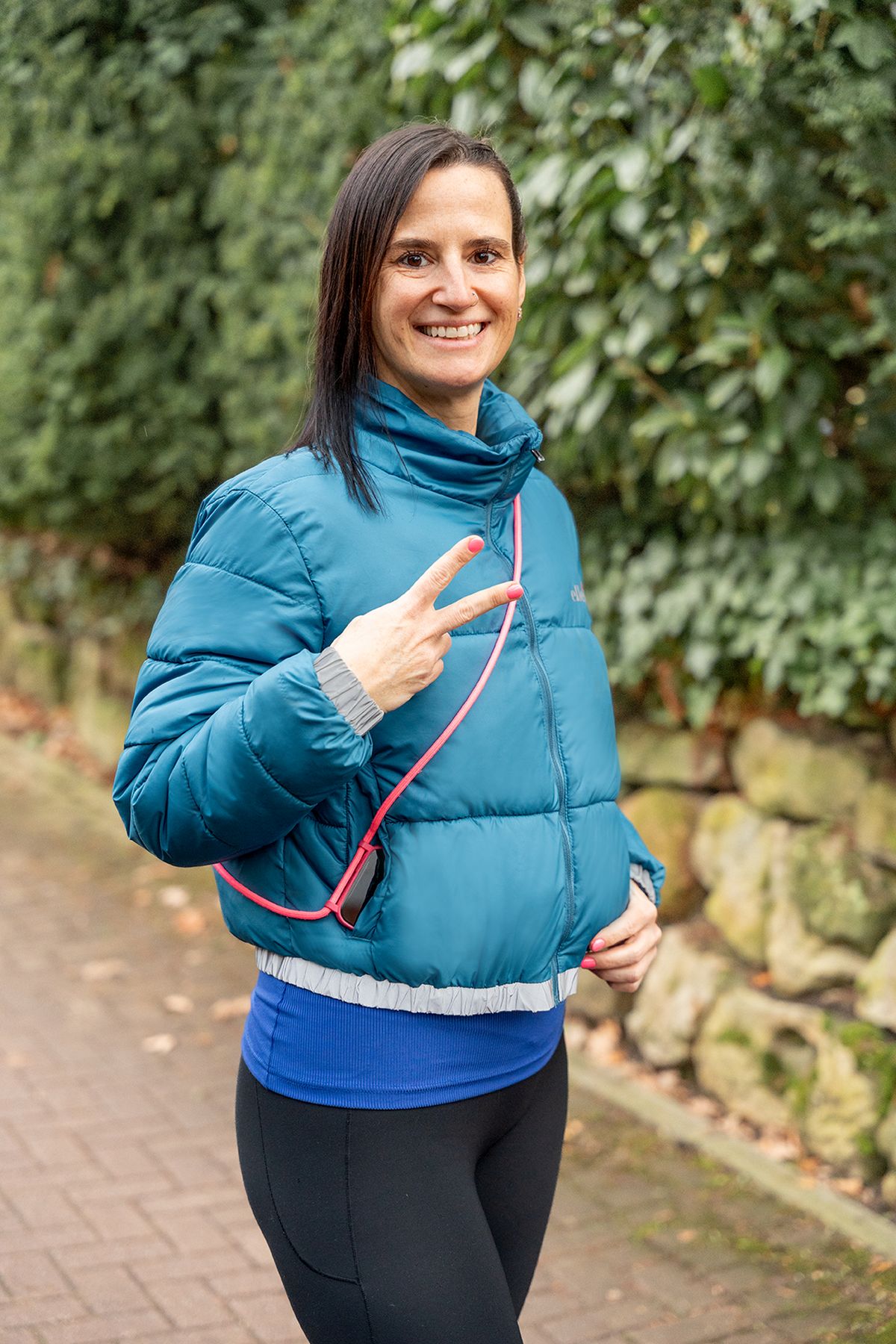 Frau in blauer Jacke mit Peace-Zeichen, die auf einem Gehweg steht.